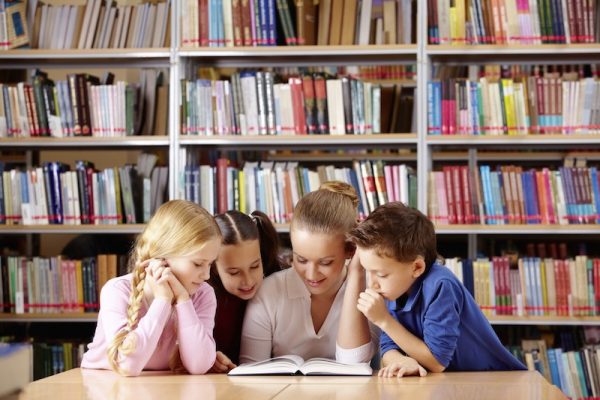 Portrait of pupils and teacher looking at page of interesting book in library